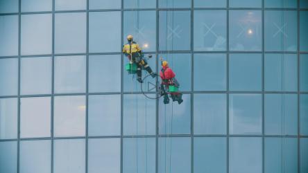 Two men in red and yellow work clothes cleaning the exterior windows of a building[4K]