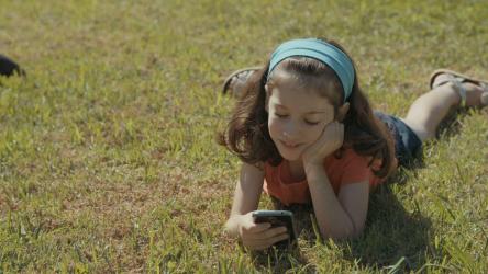 可爱的女孩躺在草地上使用手机[]