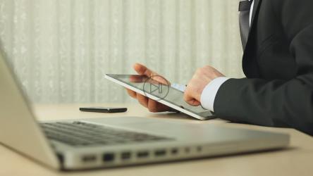 一名穿着西装的男子在电脑旁使用平板电脑[]