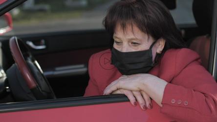 忧心忡忡的老妇人在她的车里戴着口罩[]