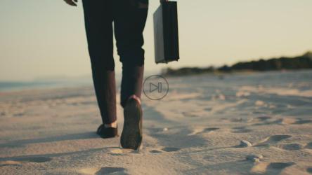 一个拿着黑色公文包的商人走在海边的海滩上。[]