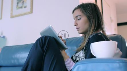 一位坐在沙发上喝咖啡的女士在浏览她的平板电脑[]