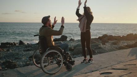 两个朋友，一个坐在轮椅上，日落时在码头上快乐[]