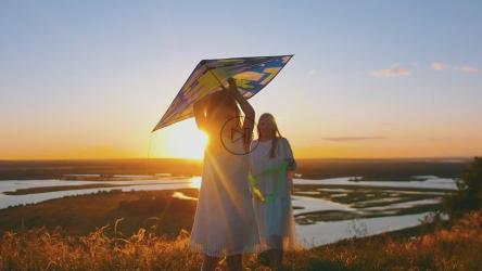 日落时，小女孩和她的妈妈拿着风筝跑步[]