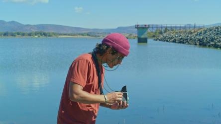 一个年轻人在湖边调整一台旧相机[免费商用]