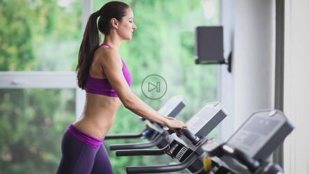 长发运动女性在健身房的跑步机上跑步[]