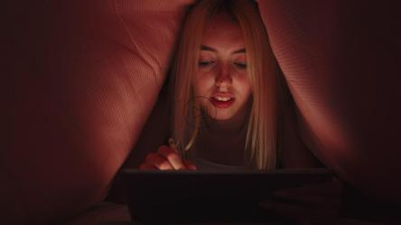 女人晚上在床罩下的平板电脑上写字[]