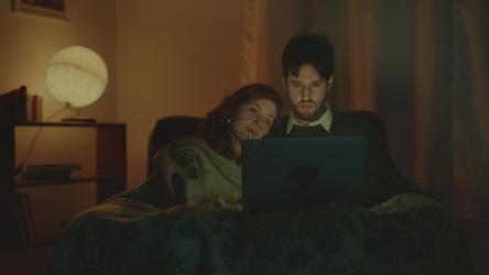 一对夫妇坐在休息室的沙发上用电脑看电影[]