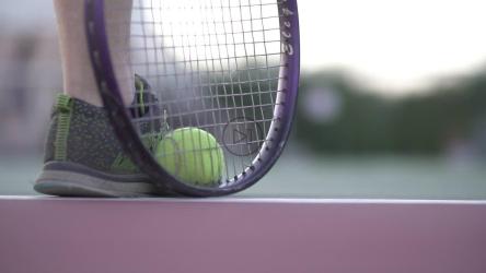Tennis player holds tennis ball against foot with racket[]