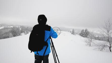 雪地里带着相机和三脚架的摄影师[]