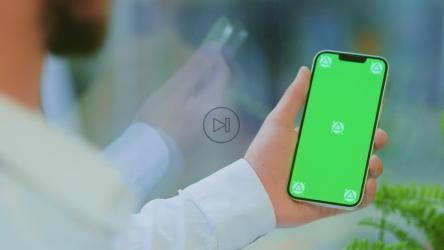 一名身穿衬衫的男子拿着一部带绿色屏幕的手机[]