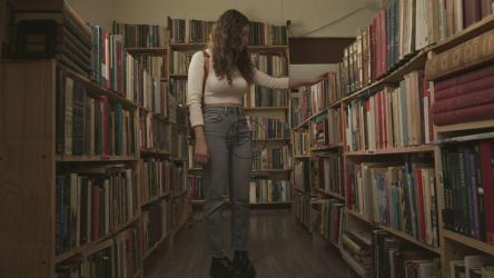 一位年轻的女学生跪下来从图书馆的书架上挑选一本书[免费商用]