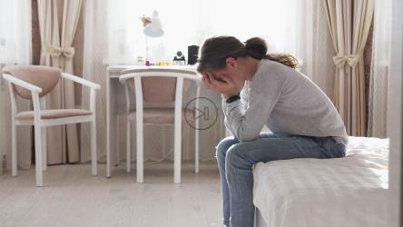 年轻女孩双手抱头坐在床尾[]