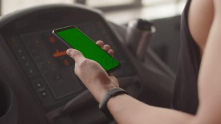 一名男子在跑步机上行走时拿着手机的特写[]