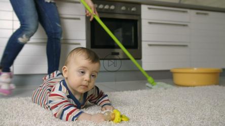 婴儿躺在地毯上，妈妈在后面打扫[]