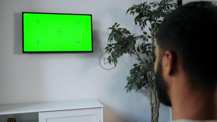 男子用遥控器指着墙上的绿屏电视[4K]
