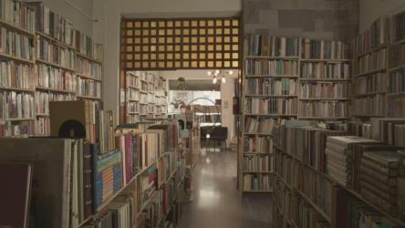 一位背着背包的年轻女学生走在图书馆的书架中间[免费商用]