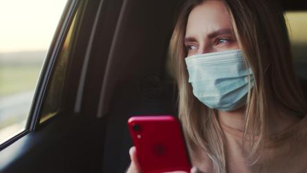 一名戴着口罩的年轻女子在出租车后座检查电话[]