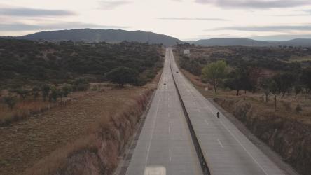 骑摩托车的人的鸟瞰图摩托车 Motorcycle:一名男子骑着摩托车在三条车道上行驶，头戴头盔，身穿黑色夹克。汽车从路的另一边驶过。下午，日落前，天空晴朗。