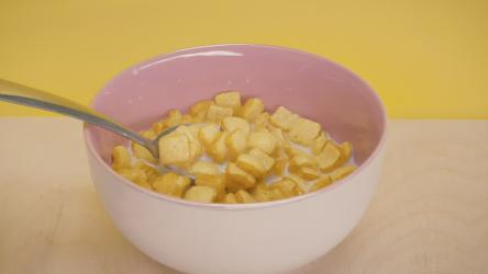 取一勺面包和牛奶形式的麦片玉米 Corn:从木桌上的碗里拿出一勺黄色背景的麦片和牛奶三明治面包。