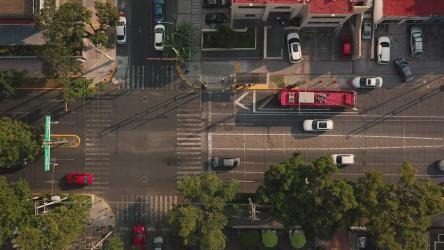 白天城市交通鸟瞰图摩托车 Motorcycle:用无人机记录的交通的高角度拍摄。汽车在单行道上驶入车流。街上停着汽车和树。