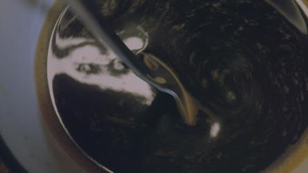 近距离观察在杯子里搅拌咖啡饮料 Drink:当一个人用勺子轻轻而缓慢地混合时，它需要非常接近一杯咖啡的内部。