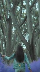 城市妇女与烟雾弹在森林烟 Smoke:一位都市时尚女性在森林中行走，在一些树旁挥舞着紫色烟雾弹。