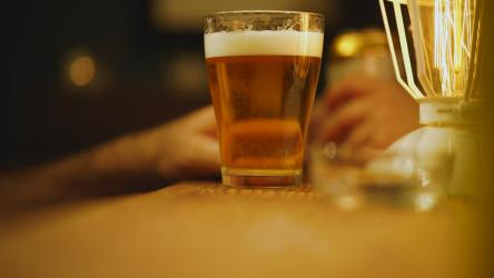 啤酒吧氛围啤酒 Beer:特别关注的是在昏暗的黄灯下，一个木棒上的一杯啤酒，里面有更多的饮料、人和一个点燃香烟的烟灰缸。