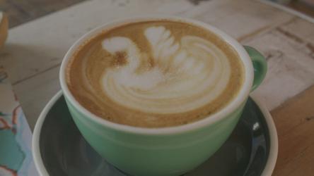 在杯子里搅拌拿铁艺术的人咖啡 Coffee:一个人在咖啡店里搅拌一个放在绿色大杯子里的拿铁艺术。