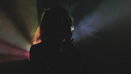 带尾灯在黑暗中吸烟烟 Smoke:一个人的剪影,吸烟时用多色尾灯照亮其轮廓,同时从嘴里排出烟雾。在电影院吸烟的人。