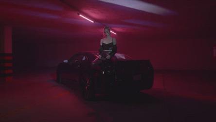 坐在跑车上的时尚女性更多 More:穿着大靴子和皮夹克的时尚女人,坐在一辆跑车上,在一个有紫色灯光的黑暗停车场里。