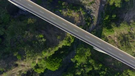 穿过郁郁葱葱的绿色景观的道路鸟瞰图更多 More:一座孤零零的桥横跨郁郁葱葱的绿色景观，其灰色的广阔与下面生机勃勃的树叶相映成趣。阳光突出了纹理和阴影，在自然和基础设施之间形成了鲜明的对比。