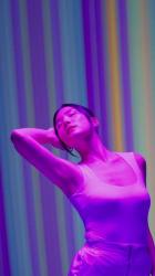 一位年轻的亚洲女舞者精彩表演的垂直视频时尚 Fashion:一位年轻的舞者在粉红色的灯光照射下，在改变形状和颜色的彩色条纹的背景上进行的丰富多彩的表演。